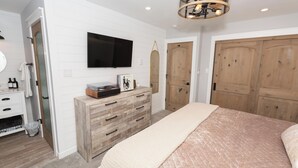 Une chambre à coucher comprenant un lit, une commode, un téléviseur et des armoires en bois.