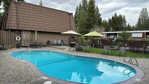 Une piscine entourée de chaises longues et de parasols, elle-même bordée d’une terrasse en briques et d’un bâtiment en bois.