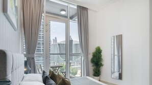 A modern bedroom with a bed, a potted plant, and a view of the cityscape through large windows.