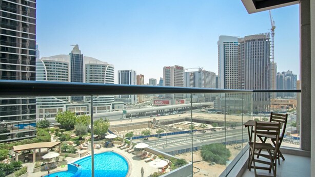 A balcony with a view of a swimming pool and cityscape.