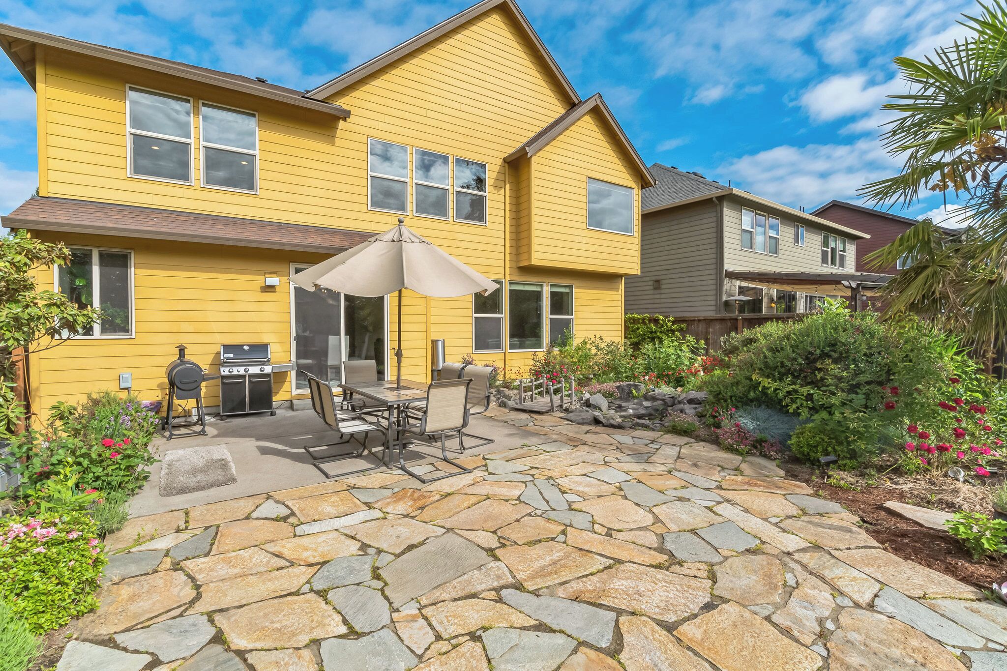 A yellow house with a stone patio, outdoor grill, and patio furniture.