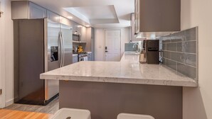 Een moderne keuken met roestvrijstalen apparatuur, een marmeren aanrechtblad en uitzicht op de woonkamer.