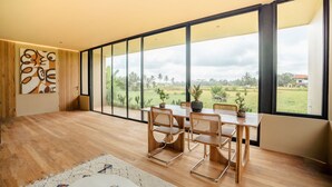 A spacious room with a large window, wooden flooring, a dining table with chairs, and a potted plant. - Hygge Villa Ubud (Ubud)