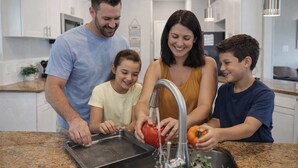 Una familia de cuatro personas en una cocina moderna con electrodomésticos de acero inoxidable, encimera de granito y un lavamanos visible.