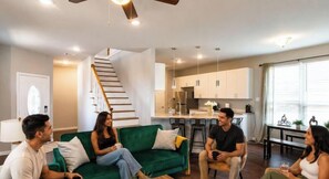 A modern living room with a green sofa, a staircase, and a kitchen in the background.
