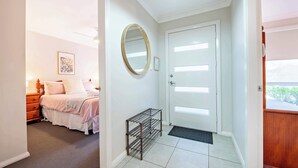 Een slaapkamer met een bed, nachtkastje, spiegel en een deur met lichtschakelaar.