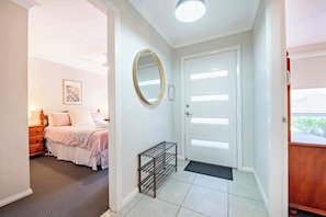 A bedroom with a bed, a bedside table, a mirror, and a door with a light switch.