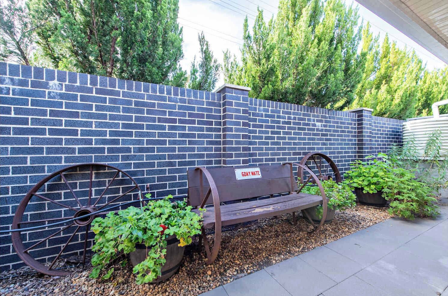 Un banc avec une plaque, un mur en briques bleues et de la verdure.
