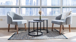 A modern room with two grey armchairs, a small round table, and a view of a cityscape through large windows. - 4bed Apt Dubai Marina Near JBR Pool by Belvilla (Dubai)