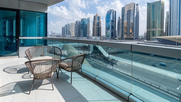A balcony with two wicker chairs, a glass railing, and a city skyline view. - 4bed Apt Dubai Marina Near JBR Pool by Belvilla (Dubai)