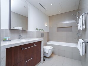 A modern bathroom with a large mirror, a vanity with a sink, a toilet, and a bathtub.