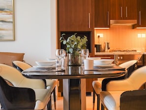 A modern dining area with a round table set for four, surrounded by leather chairs. A vase with greenery is placed in the center.