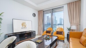 A modern hotel room with a city view, a flat-screen TV, a dining table, two yellow armchairs, and a sofa. - Lux 1BR Apt Burj Khalifa View by Belvilla (Dubai)
