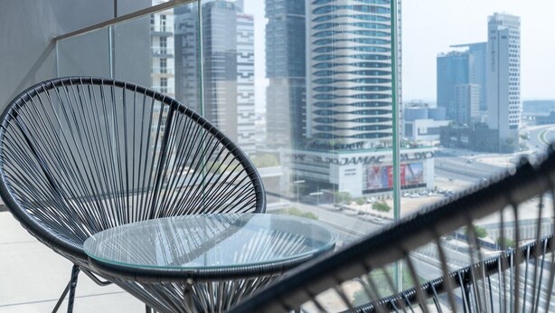 A modern chair with a glass table in a high-rise building with a city view. - 1BR Dlx City View Near Dubai Mall by Belvilla (Dubai)