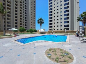 Ein Pool, umgeben von einer angelegten Grünfläche mit Palmen und Liegestühlen.