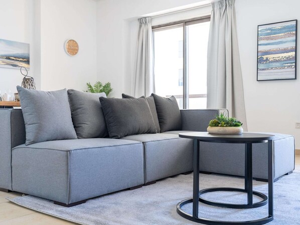 Ein modernes Wohnzimmer mit einem grauen Ecksofa, einem runden schwarzen Couchtisch, einem kleinen Topfpflanzen und einem Gemälde an der Wand.