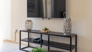 Un salón moderno con un televisor de pantalla plana montado en la pared, una mesa consola negra con objetos decorativos y un enchufe en la pared.
