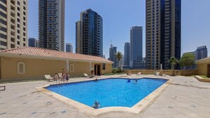 Una piscina rodeada de edificios altos, con algunas personas y tumbonas.