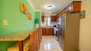 A kitchen with a dining area, wooden cabinets, a refrigerator, and a water dispenser. - Garden Condos 40, 1br Apt In Sosua Strip! Guest Ok (Sosúa)