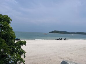 Une plage avec un ciel dégagé, une mer calme et une île qui se profile à l’horizon.