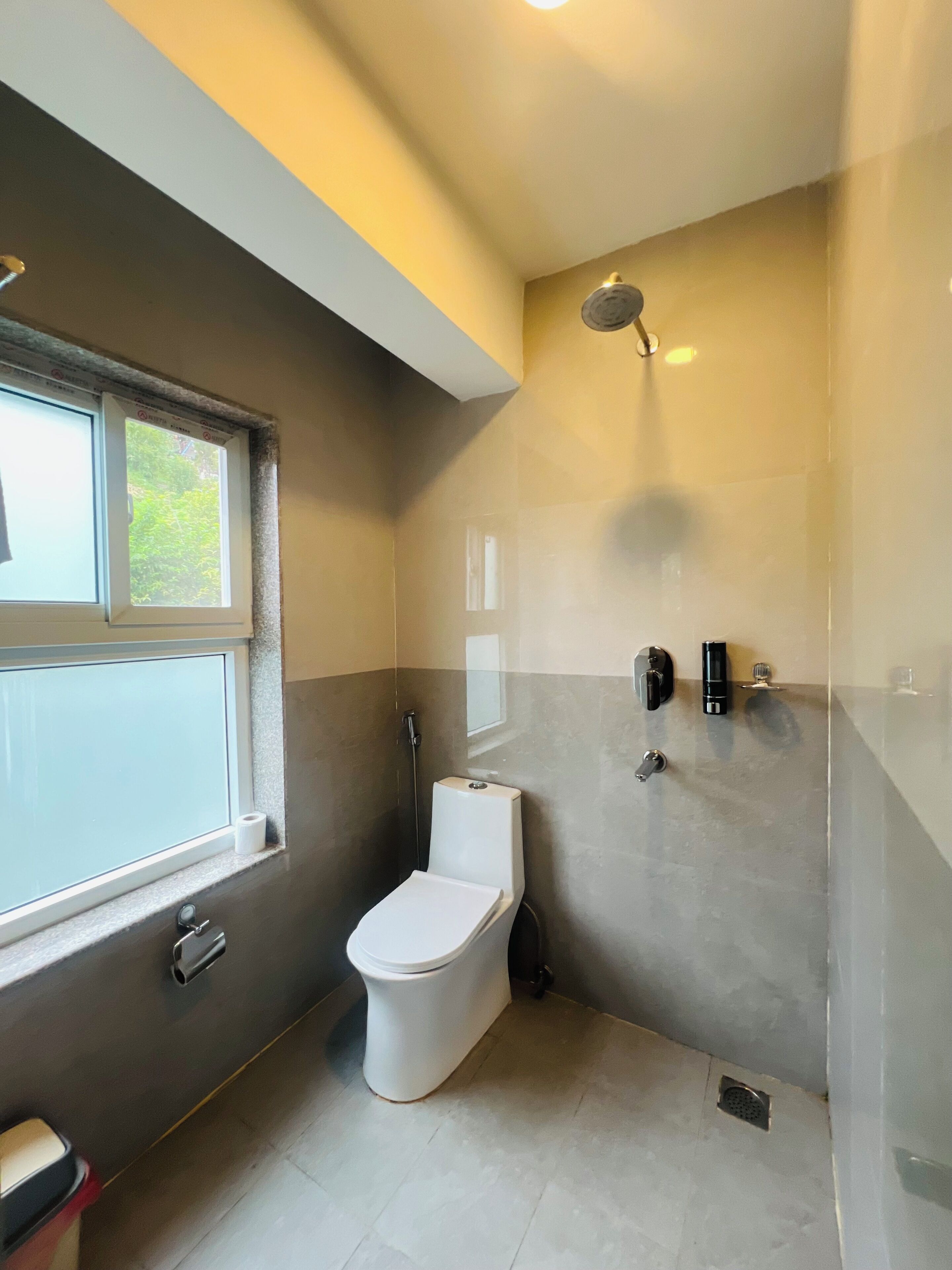 A bathroom with a toilet, a shower, and a window.
