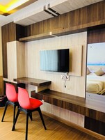 Una habitación moderna con televisor de pantalla plana en pared de madera, un escritorio pequeño con una silla y una cama con vistas.