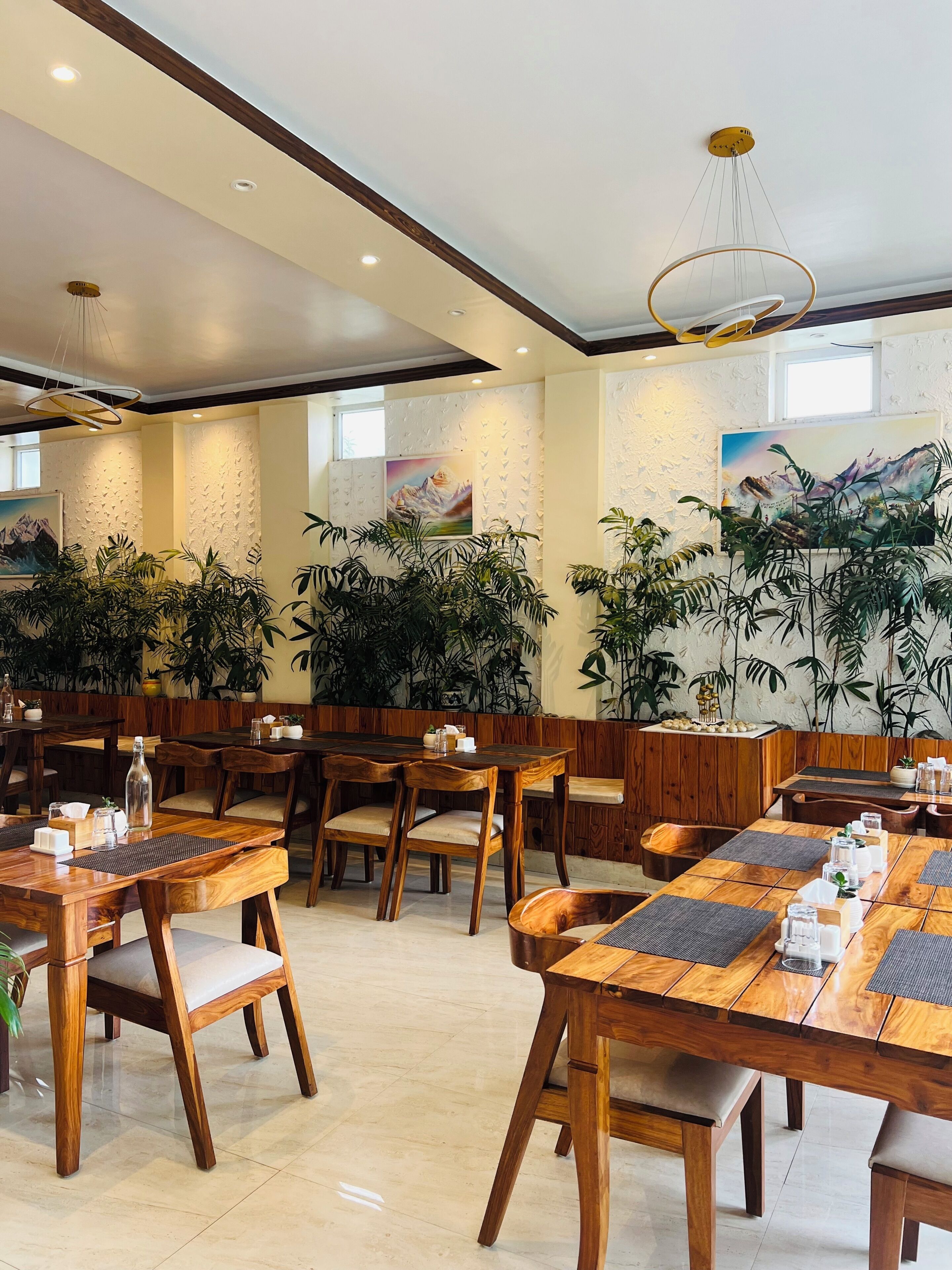 A restaurant with wooden tables and chairs, potted plants, and artwork on the walls.