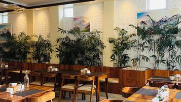 A restaurant with wooden tables and chairs, potted plants, and artwork on the walls.