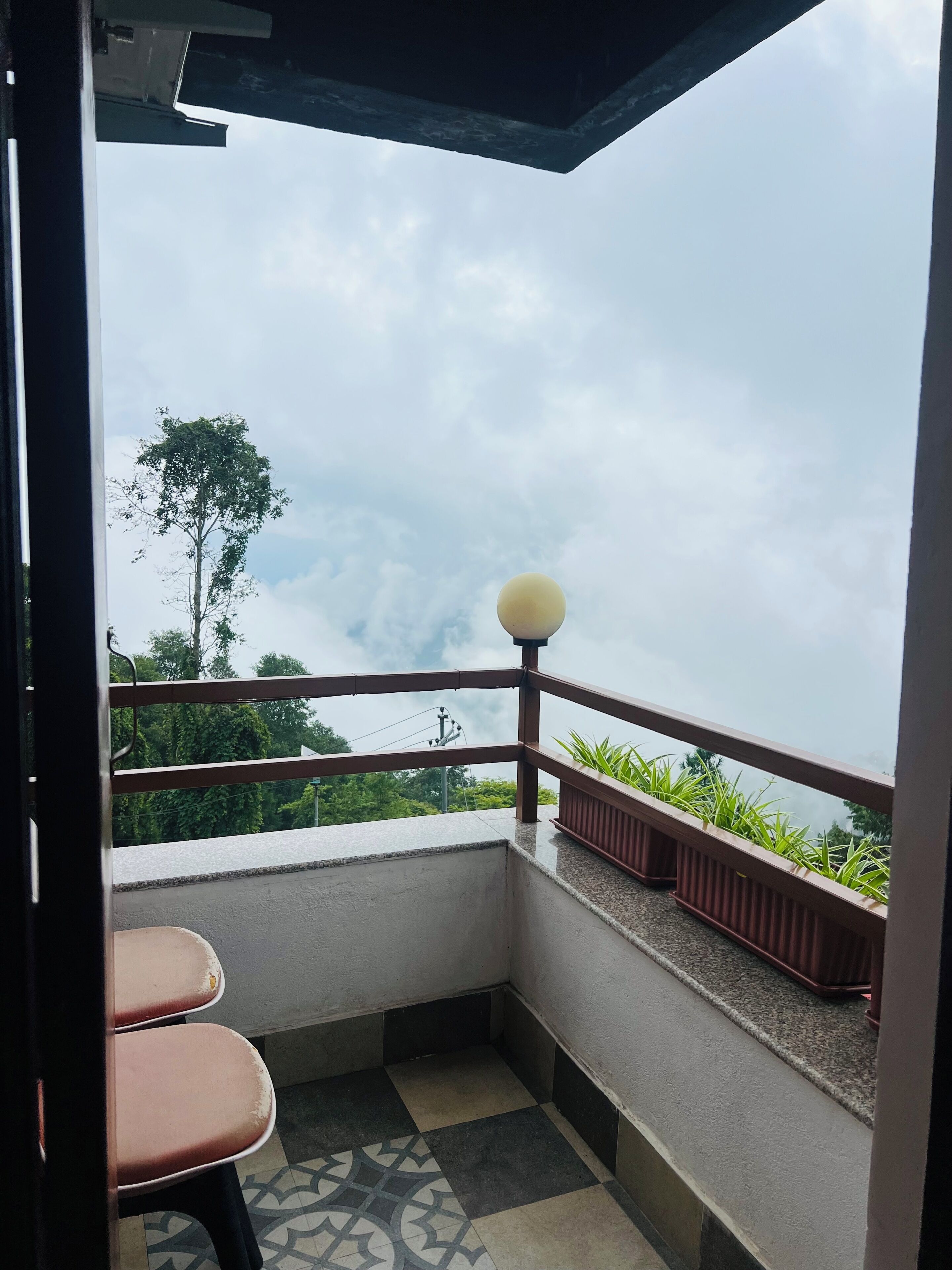 A balcony with a view of the sky and trees, a railing, and a table with chairs.