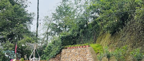 Un espacio al aire libre con mesas y sillas, rodeado de plantas en macetas y un muro de piedra.