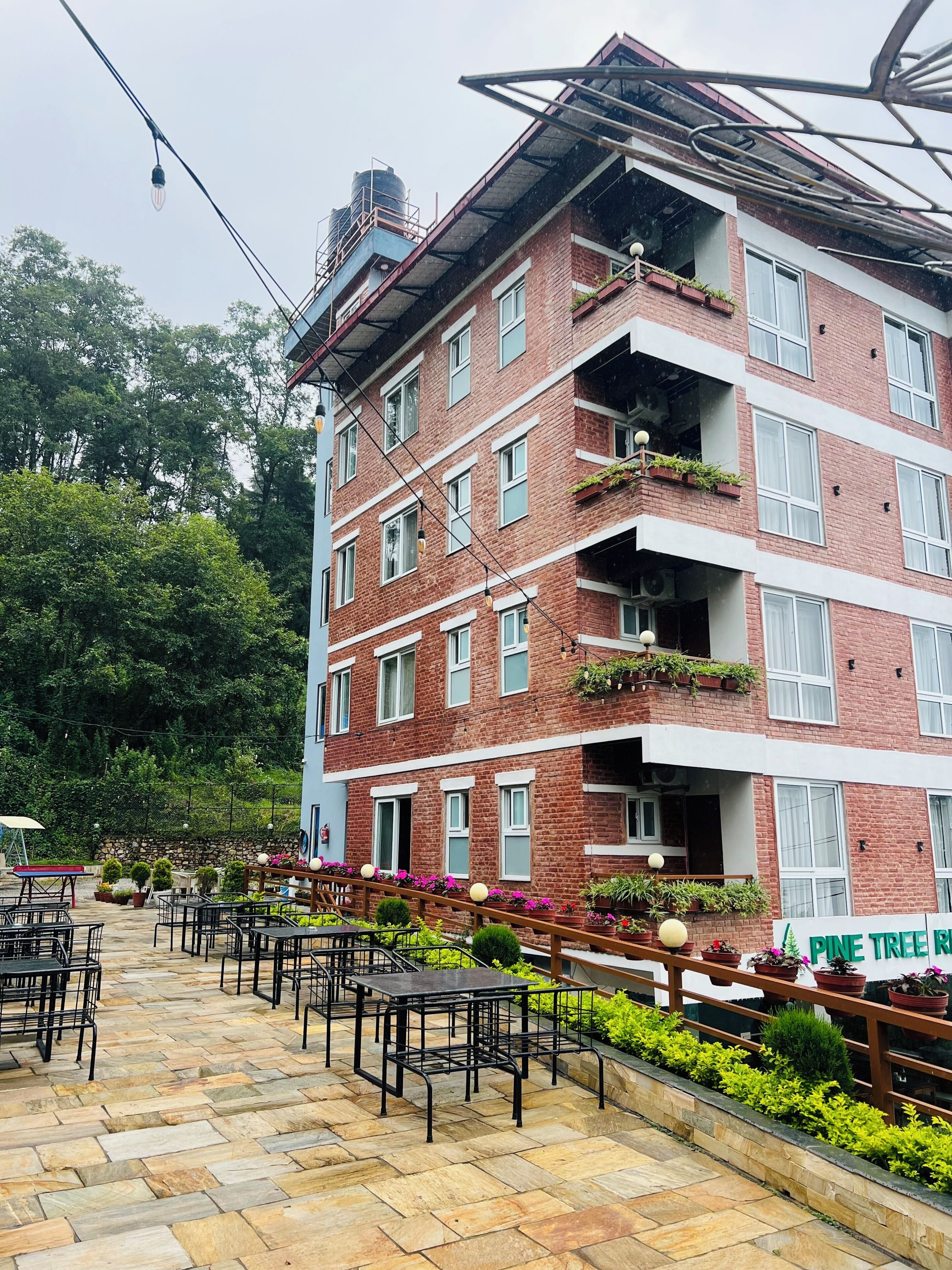 A multi-story building with a brick facade, outdoor seating area, and potted plants.