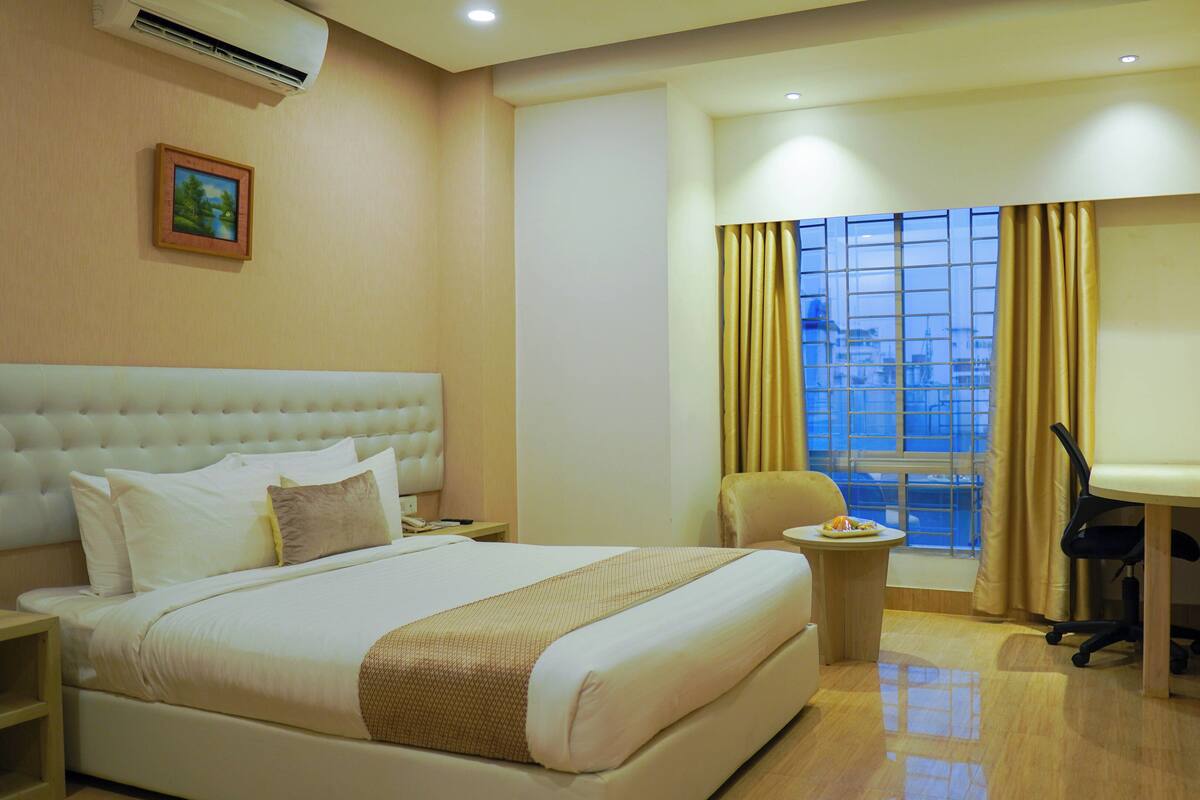 A hotel room with a large bed, a desk, a chair, a TV, and a window with curtains.