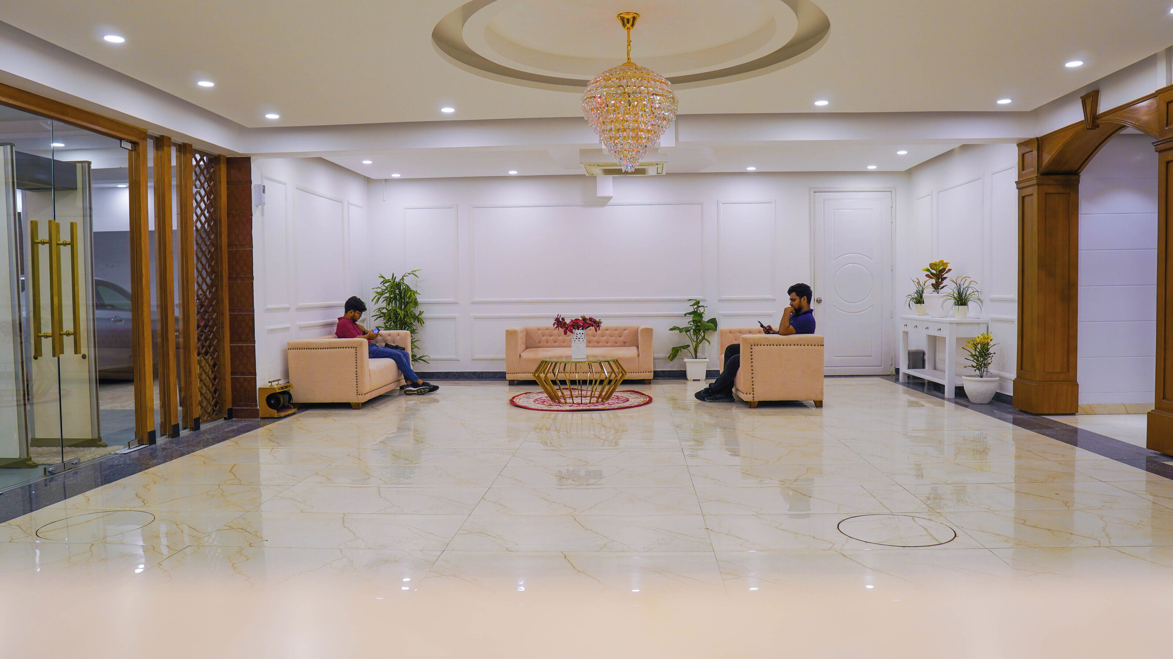 A spacious lobby with a marble floor, two sofas, a central table, and a decorative chandelier.