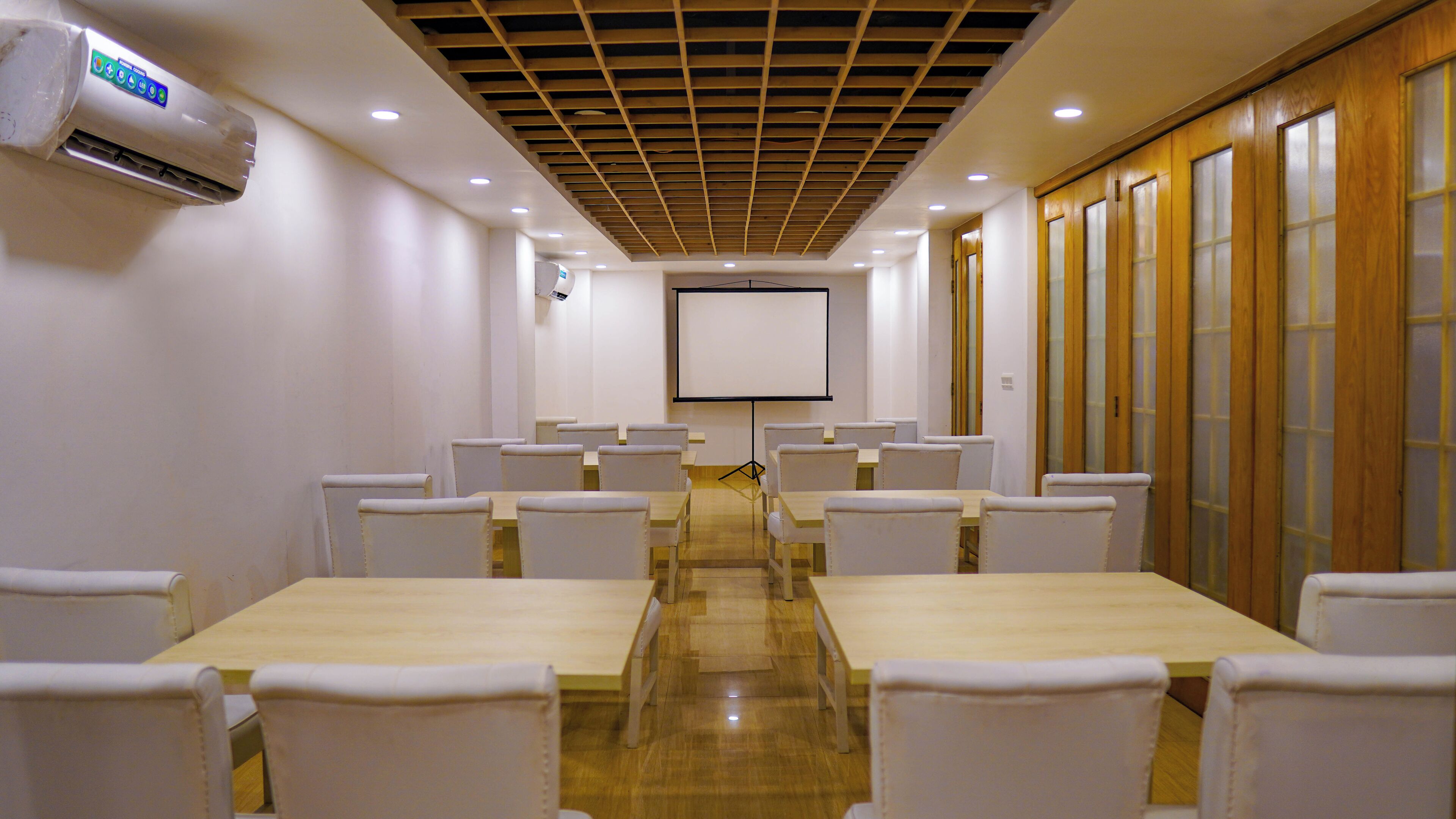A conference room with a long table, white chairs, a projector screen, and an air conditioning unit.