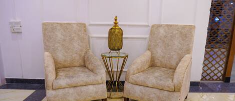 Deux fauteuils recouverts d’un tissu texturé, une petite table ronde avec un plateau en verre et des pieds dorés, et un vase décoratif posé sur la table.