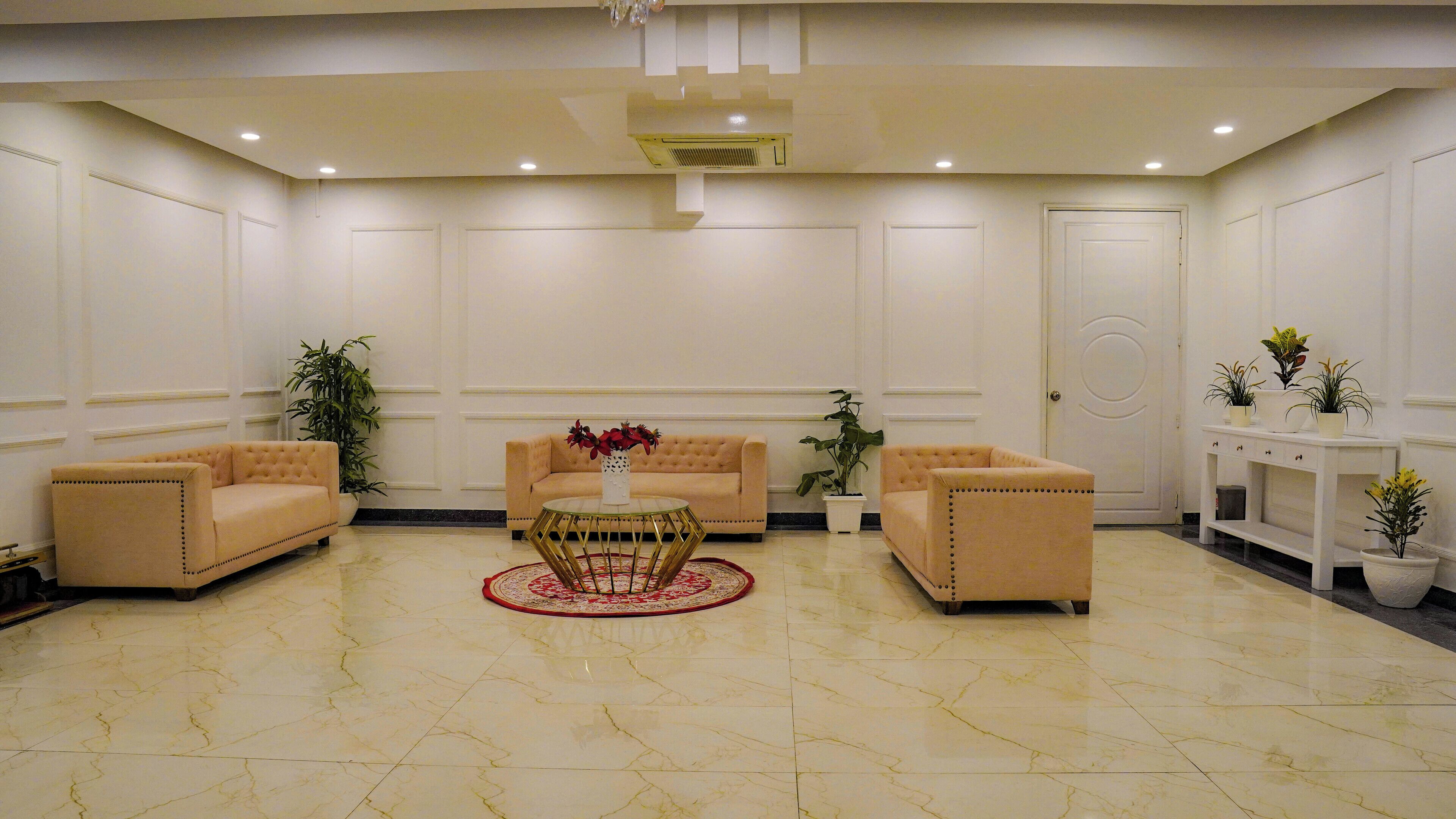 A spacious lobby with a marble floor, two sofas, a coffee table, and a potted plant arrangement.