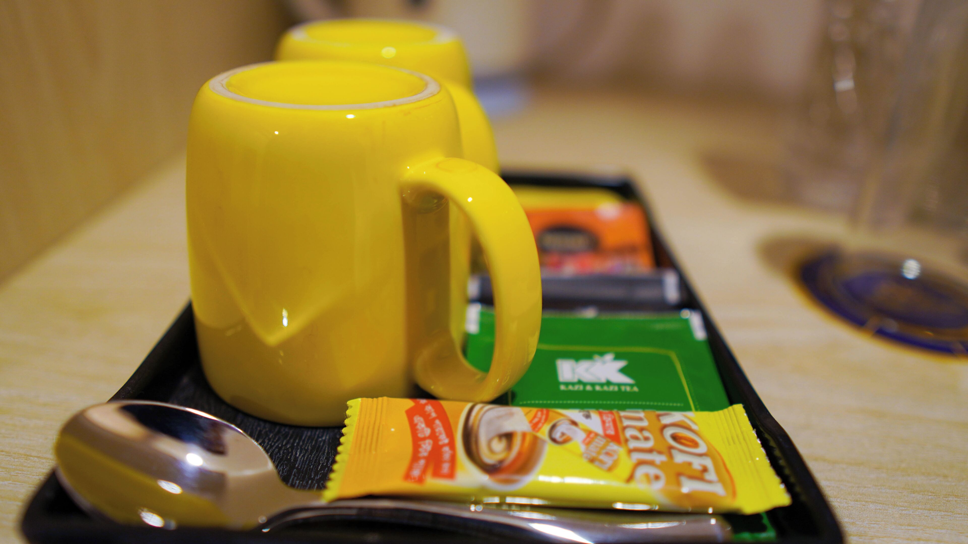 A tray with yellow mugs, a spoon, and a packet of instant coffee.