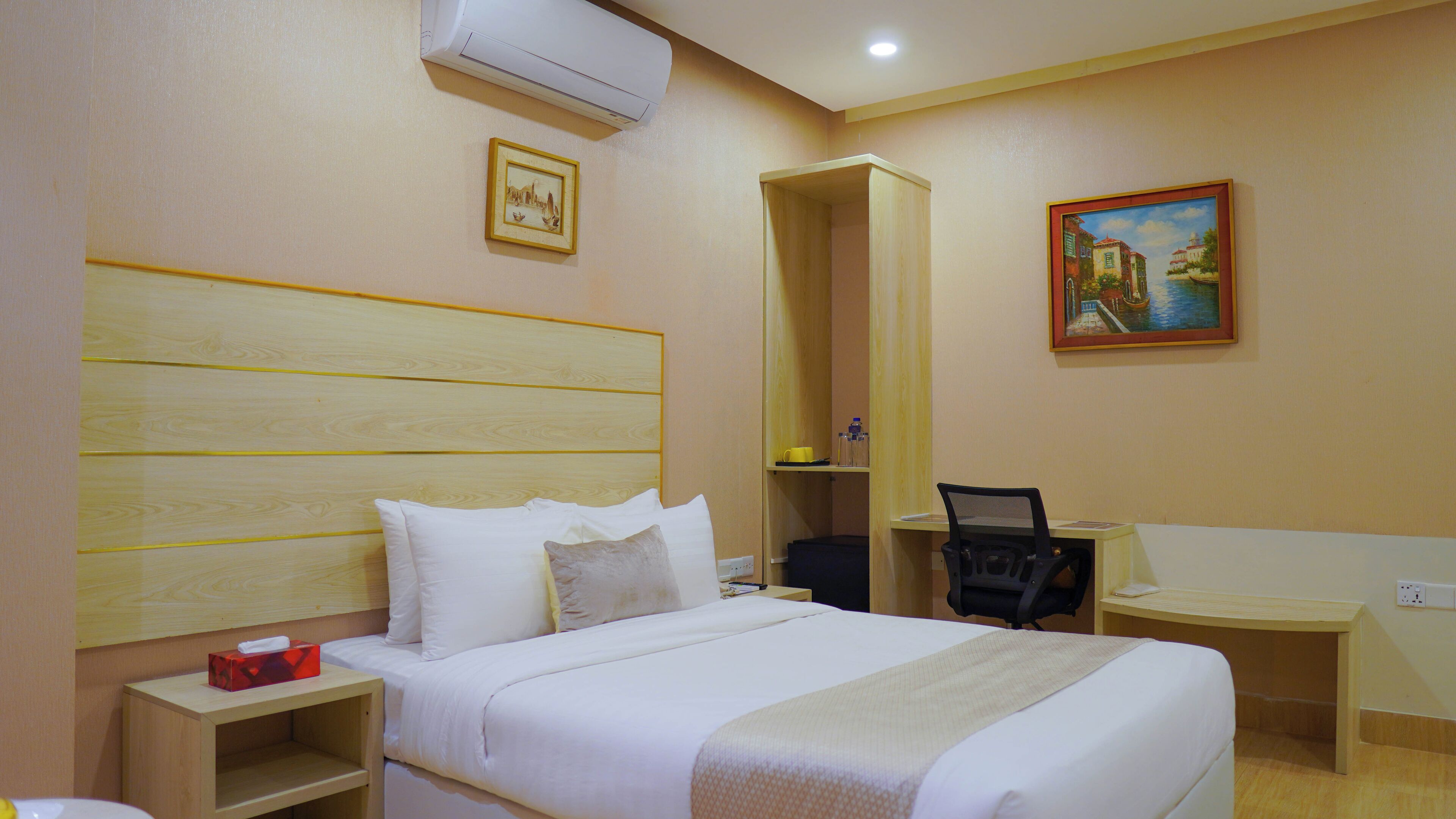 A hotel room with a large bed, a desk, a chair, and a painting on the wall.