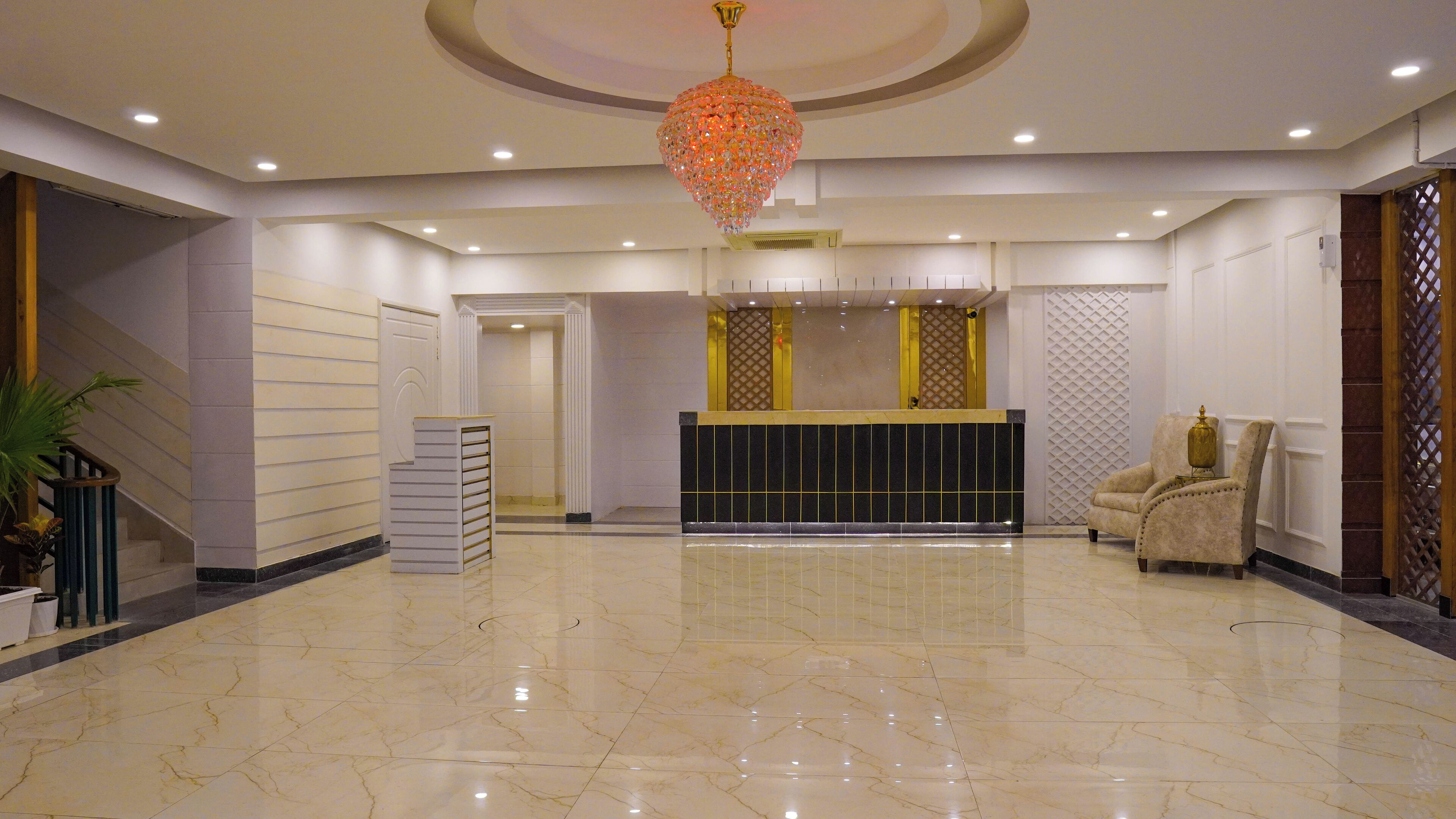 A spacious lobby with a marble floor, a reception desk, a decorative chandelier, and a seating area.