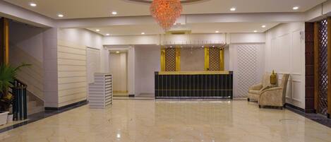 A spacious lobby with a marble floor, a reception desk, a decorative chandelier, and a seating area.