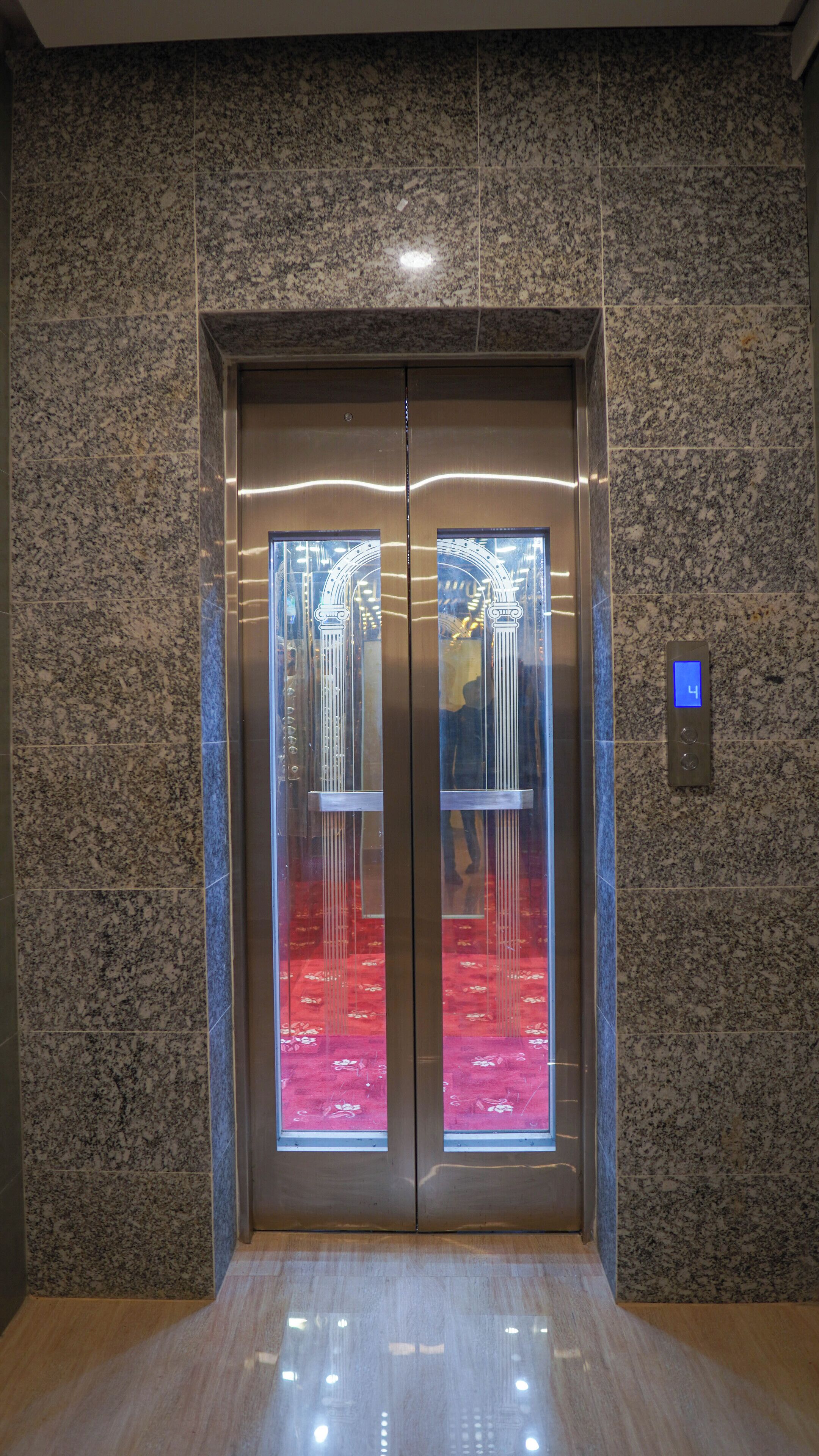 An elevator with a digital display showing the number 4, surrounded by granite walls and a polished floor.