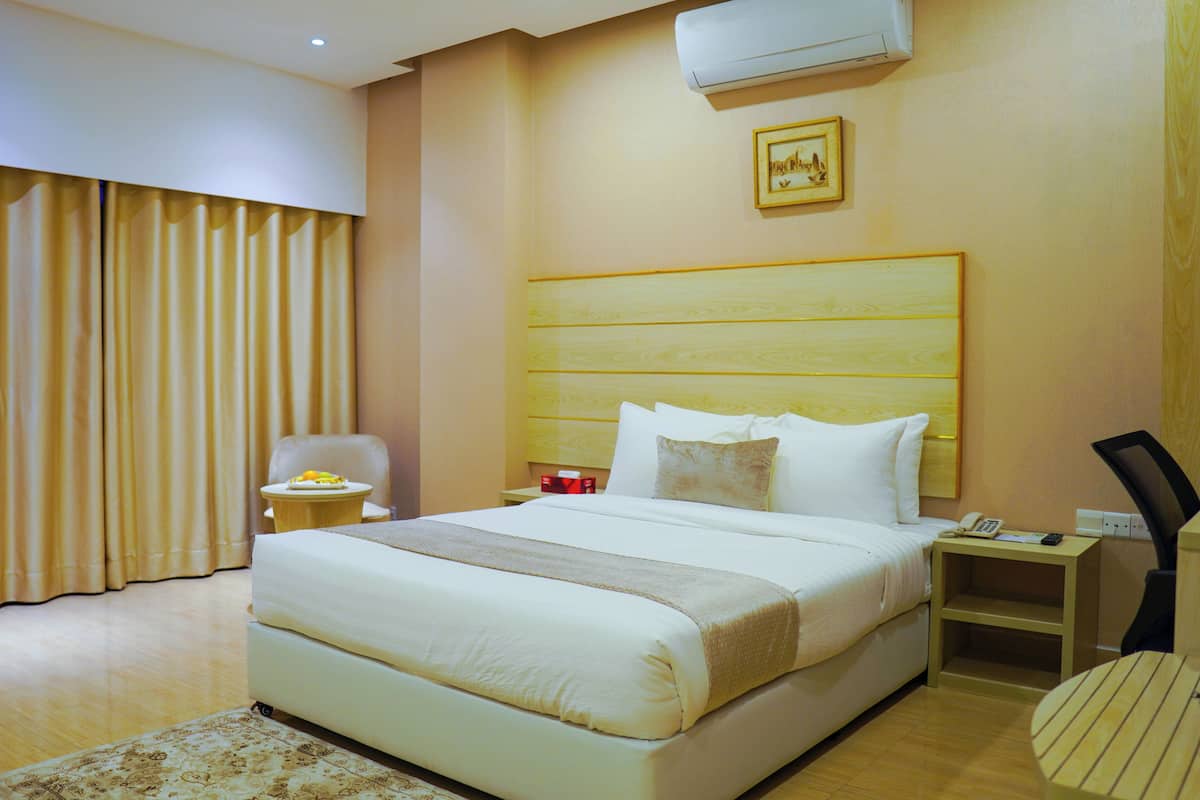 A hotel room with a large bed, a bedside table with a phone and a lamp, a chair, a small table with a plate of food, and a picture on the wall.