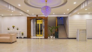 A spacious lobby with a marble floor, a large chandelier, a staircase, and a reception desk. - Grand Vistana (Dhaka)