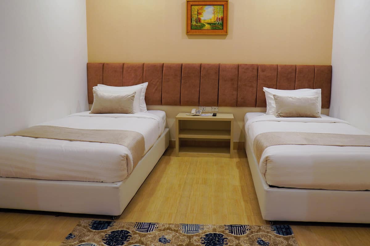 A hotel room with two beds, a small bedside table with a phone and remote, and a painting on the wall.