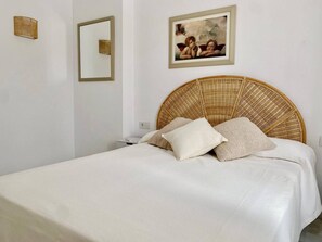 A bed with a wicker headboard, white bedding, and two pillows.