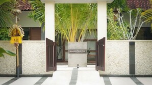 Entrada de un hotel con pared de piedra, portón de madera y un letrero que dice "MAHADINUSA".