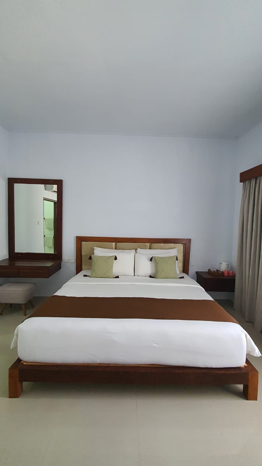 Una habitación de hotel con una cama grande, un cabecero de madera, un espejo, una mesita de noche y un tocador.