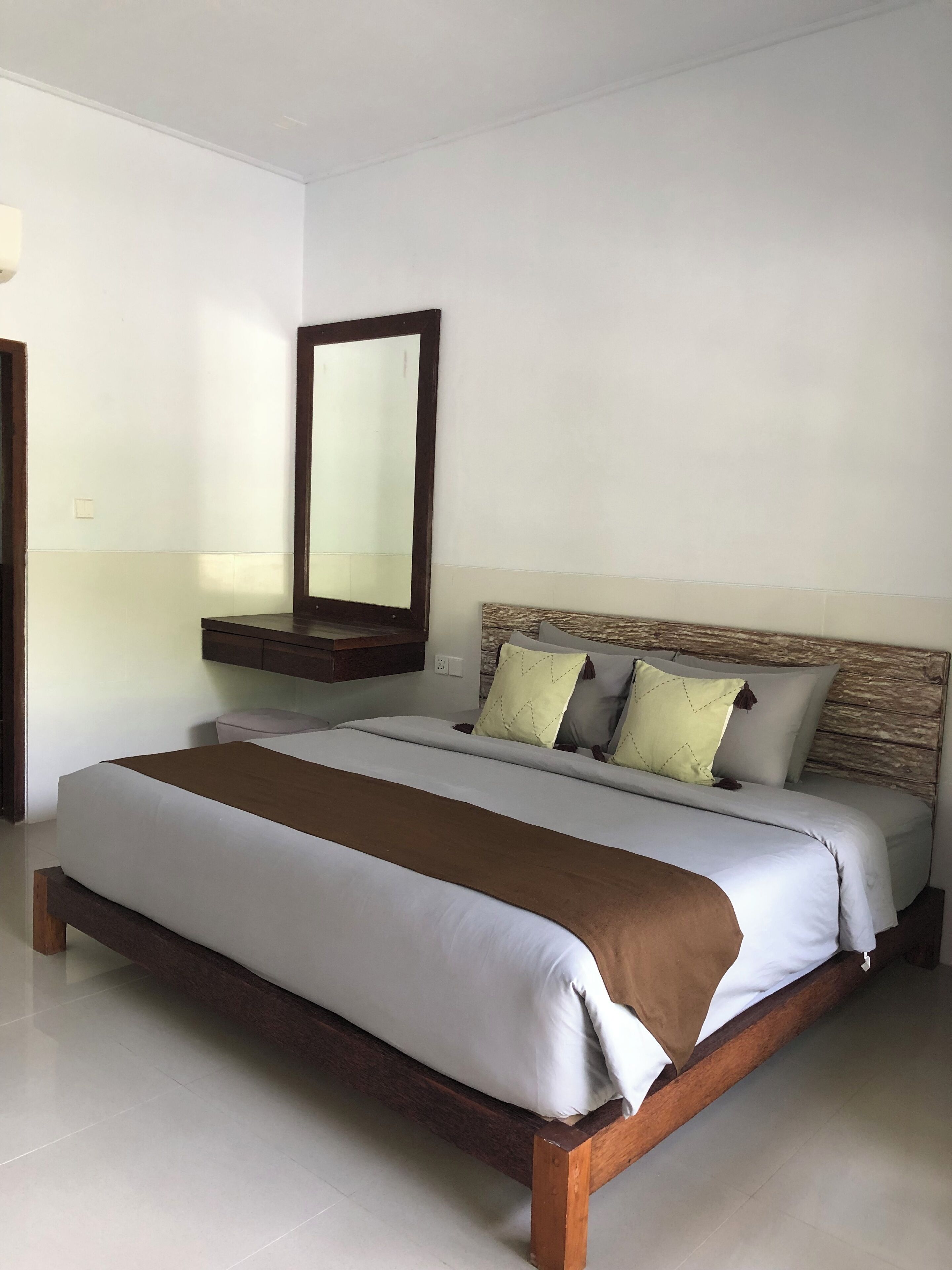 A neatly made bed with a wooden headboard, a large mirror above it, and a bedside table with a lamp.