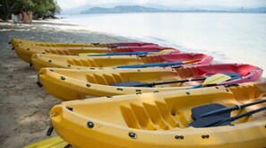 A row of yellow and red kayaks lined up on a sandy beach with a calm body of water and mountains in the background. - OYO 90980 Rainbow Island Sepanggar (Sepanggar Island)