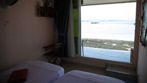A room with two beds, a window with a view of the sea, and a small table with a chair. - OYO 90980 Rainbow Island Sepanggar (Sepanggar Island)